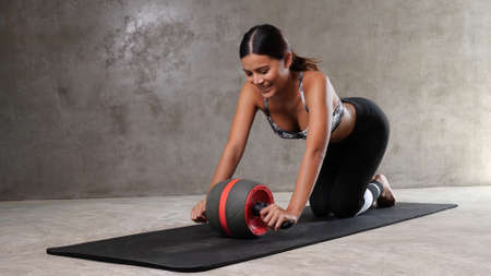 Beautiful young Asian woman exercising with ab wheel on the yoga mat at the gym. Happy girl spending her free time at the sport centreの写真素材