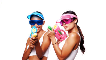 Portrait of two beautiful Asian women in pink and blue sun visor cap and sunglasses posing with water guns over white backgroundの写真素材