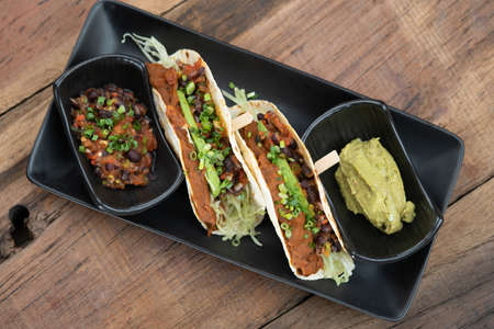 Baked tortillas with black beans, tomato, cilantro, red onion, avocado and assorted spices served with avocado dip on the sideの写真素材