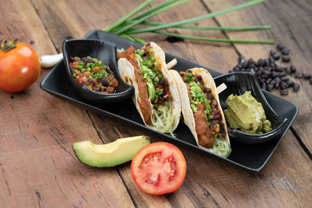 Baked tortillas with black beans, tomato, cilantro, red onion, avocado and assorted spices served with avocado dip on the sideの写真素材