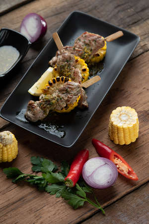 Spiced grilled pork tenderloin with a mint sauce served with lemon and sour cream on the side isolated on the wooden tableの写真素材