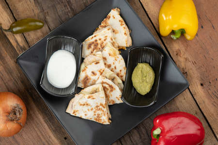 A toasted tortilla with chicken, peppers, red onion and mozzarella served with a guacamole dip and sour cream isolated on wooden tableの写真素材