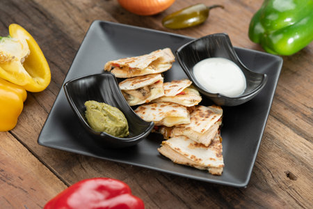 A toasted tortilla with chicken, peppers, red onion and mozzarella served with a guacamole dip and sour cream isolated on wooden tableの写真素材