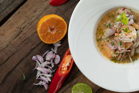 Prawns, white snapper, squid, salmon in a spicy orange dressing isolated on the wooden tableの写真素材