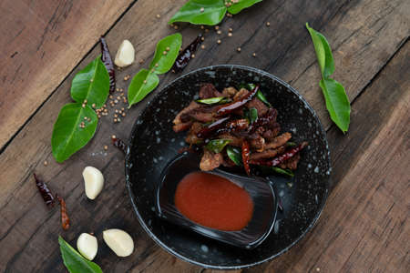 Moo ded deaw - deep fried dried pork with chilli and sriracha sauce isolated on the wooden tableの写真素材