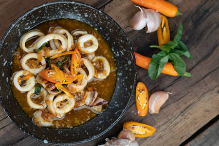 Stir-fried squid in spicy chili, garlic and basil sauce isolated on wooden rustic tableの写真素材