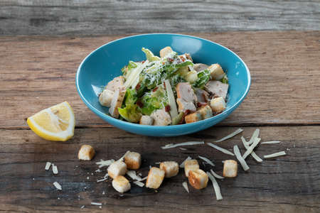 Chicken Cesar salad with croutons, grated cheese and lemon isolated on wooden rustic tableの写真素材