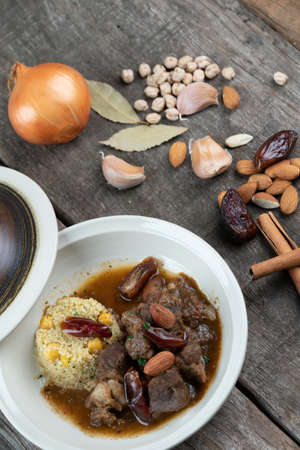 Slow cooked lamb with potato and dates served with warm couscous and chickpeas isolated on the wooden tableの写真素材