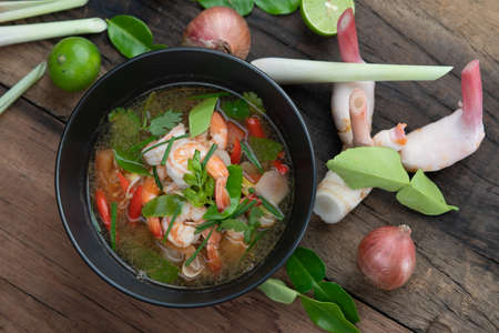 Traditional spicy prawn soup with galangal, lemongrass, kaffir lime leaf and straw mushrooms isolated on the wooden tableの写真素材