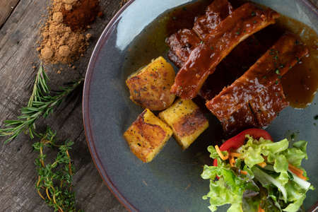 Slow baked pork cooked in brown sugar, cumin, smoked paprika and garlic powder in bbq sauce served with potatoes and salad isolated on the wooden tableの写真素材