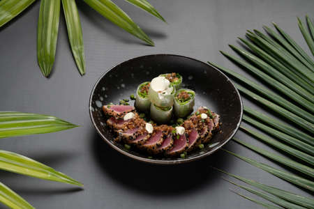 Seared tuna sesame and fresh spring rolls with ginger sesame soy sauce isolated on black table with tropical leavesの写真素材
