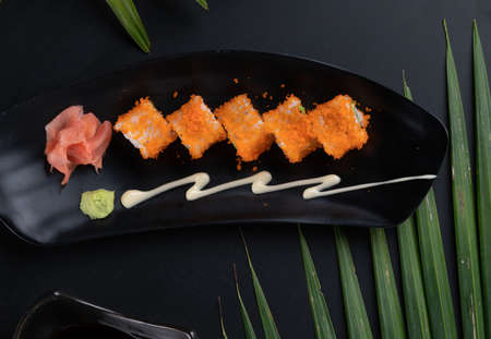 Top view of avocado, crab stick, cucumber, mayonnaise and ebiko sushi isolated on black table with tropical leavesの写真素材