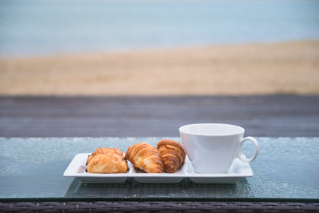 Coffee and croissants on the table with sea backgroundの写真素材