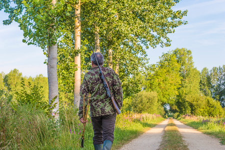 Rear view of a hunter with a gun standing on a country road