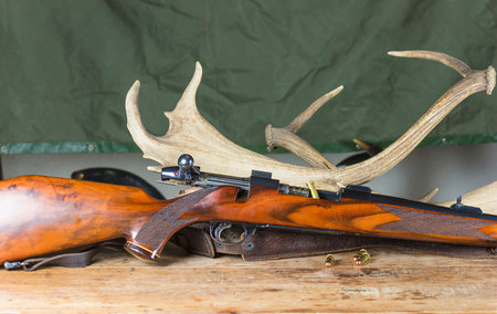 Hunting trophy with antlers and shotgun on a wooden table.