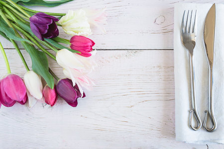 Tulips and cutlery on a white wooden background.