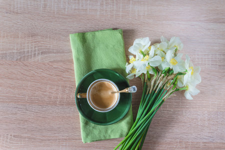 Cup of coffee and white daffodils on wooden table
