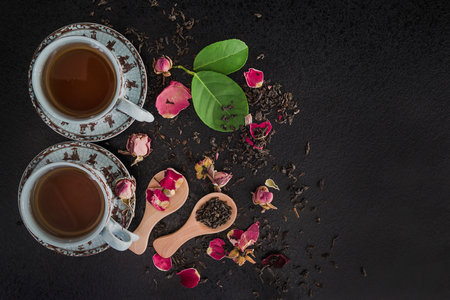 Cup of tea with rose petals and green leaves on black backgroundの写真素材