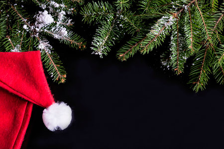 Christmas background with santa hat and fir tree branches on black backgroundの写真素材