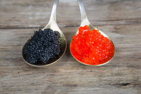Black and red caviar in a spoon on wooden background. Selective focus.の写真素材