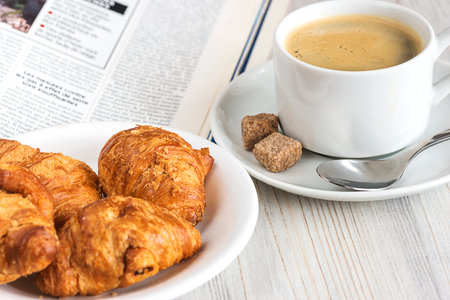 Breakfast with coffee, croissants and newspaper on wooden tableの写真素材