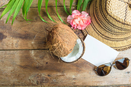 Coconut, straw hat, sunglasses and palm leaves on wooden backgroundの写真素材