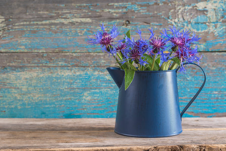 Bouquet of cornflowers in a blue watering can on a wooden backgroundの写真素材