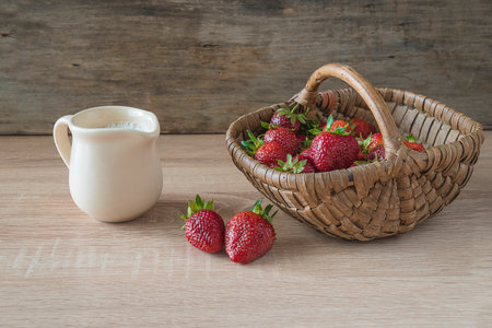 Fresh strawberries in a basket and a jug of milk on a wooden backgroundの写真素材