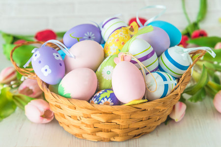 Easter eggs in a basket and pink tulips on a white wooden background