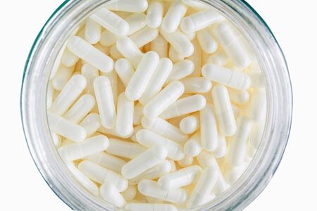 White medicine or supplement capsules in a glass. Top view.