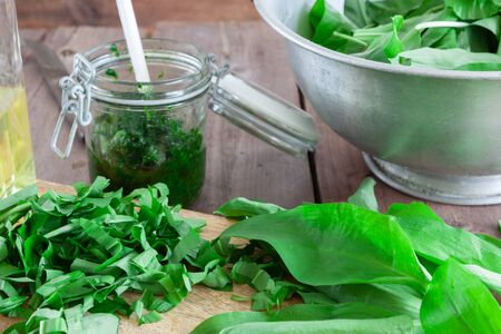 Fresh green ramson with a glass of pesto and a bowl on wooden background.の写真素材