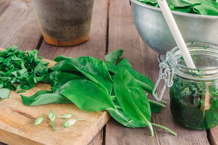 Fresh green ramson with a glass of pesto and a bowl on wooden background.