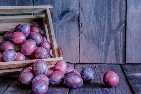 Wooden crate with plums on a wooden background with copyspace.の写真素材
