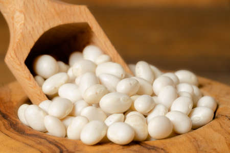 Closeup of little white dry beans in a bowl with a scoop. Dried white beans in a wooden bowl on...