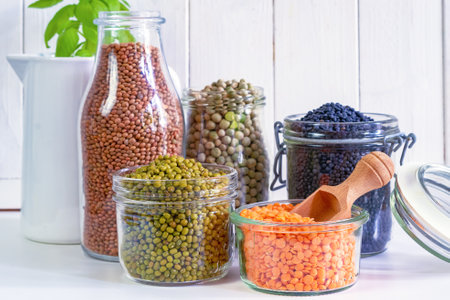 Assortment of colorful legumes in jars and glasses on a light kitchen table.の写真素材