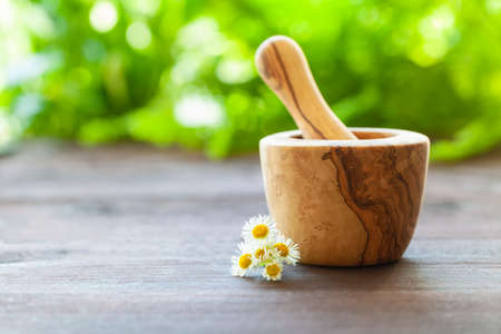 Homeopathic concept. A wooden mortar and pestle with calendula on a wooden table. A blurry green background.の写真素材