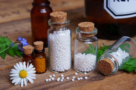 Medical glas vials on wooden table, filled with globulis. Decoratet with leaves and flowers.の写真素材