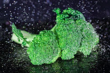 Fresh broccoli surrounded by many drops of water on black background