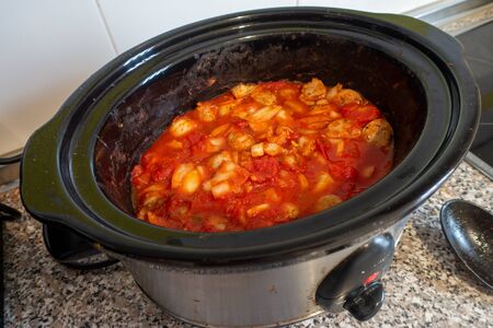 slow cooker meal of sausage, onion and tomato bubbling away on kitchen work topの写真素材
