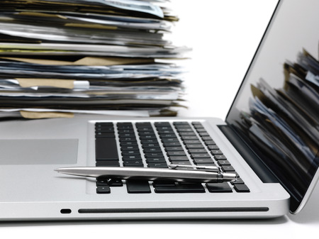 Laptop with a pile of files in background