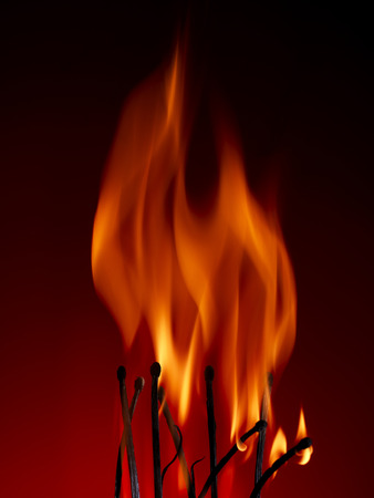 Macro shot of a flaming matchstick on a red backgroundの写真素材