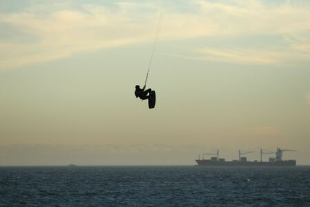 A kite surfer hangs high above the water with a container ship in the backgroundの写真素材
