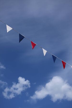 red, blue and white flag bunting flies in blue summer sky. Bright white fluffy cloudsの写真素材