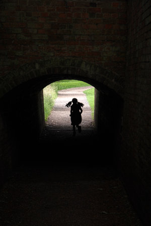 Young girl silhouette running towards the light in a tunnel under a bridgeの写真素材