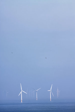 Wind turbines off the coast of North Wales, UK in blue hazy background of sea and skyの写真素材