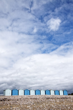 Row of beach huts at British seaside under cloudy blue summer sky. These beach huts were on a pebble beach of a holiday resort in Dorset, UKの写真素材