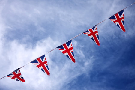 Bunting made of fabric UK Union Jack flags flies in a blue summer sky. The bunting was suspended between buildings on the high street of a seaside town in Devon, England, UKの写真素材