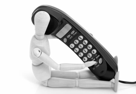 wooden figure holding a black telephone over a white backgroundの写真素材