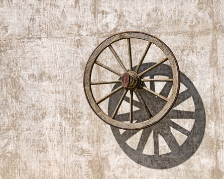 An old wooden wagon wheel casts a shadow on a concrete wallの写真素材