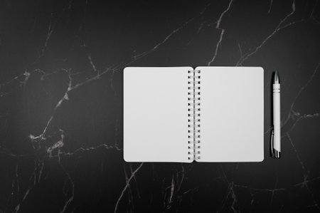 Top view of white notebook and pen on black marble background. Flat lay, copy space.の写真素材